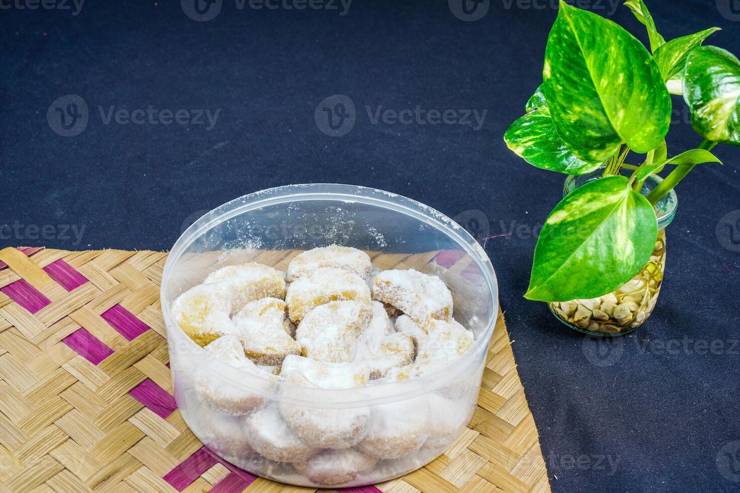 snow white cake isolated on a bamboo woven table with a black background. crescent moon cake with granulated sugar sprinkles isolated on a black background. Eid cake concept. photo