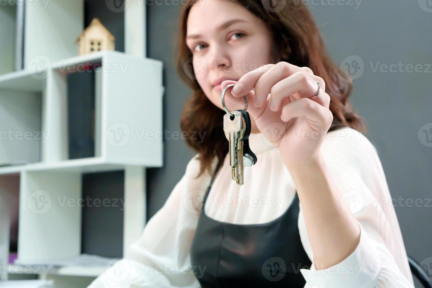 encantador niña con Rizado pelo con llaves en mano sentado a su escritorio, consiguiendo Listo a ayuda su clientela encontrar el Perfecto hogar y hacer su Sueños ven cierto foto