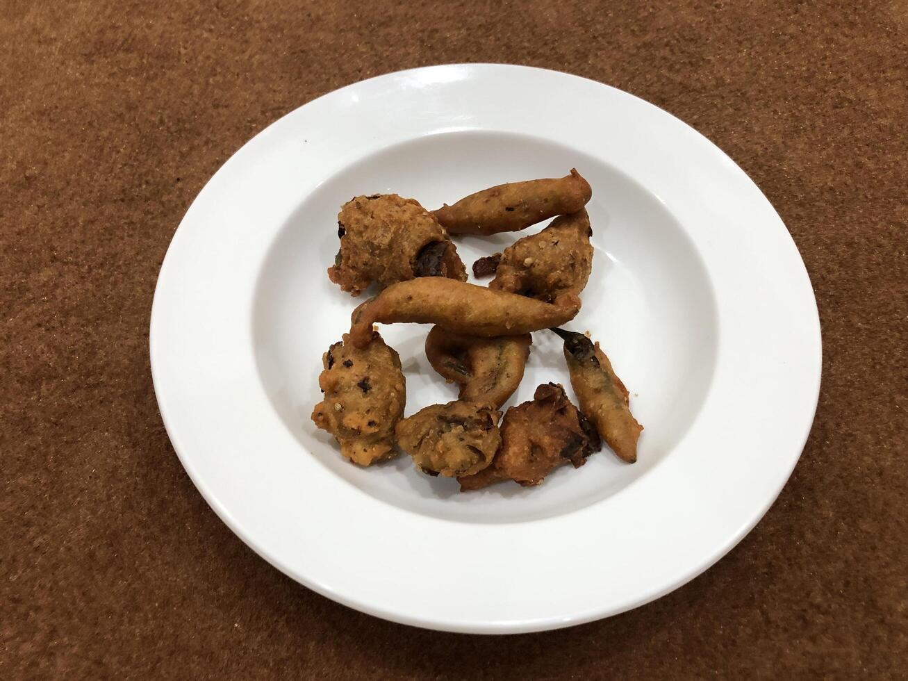 Mirchi pakora or Mirchi bhajji served in a white plate, a famous midday snack in india, served over a rustic wooden background, selective focus photo