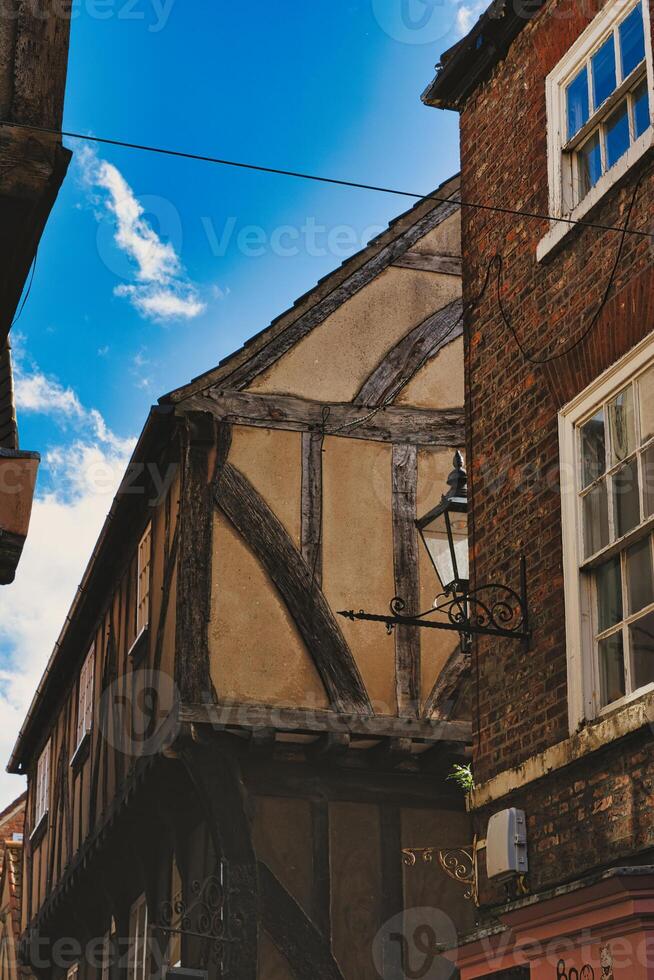 Quaint half-timbered building with exposed wooden beams under a clear blue sky, showcasing traditional architectural details and a vintage street lamp in York, North Yorkshire, England. photo