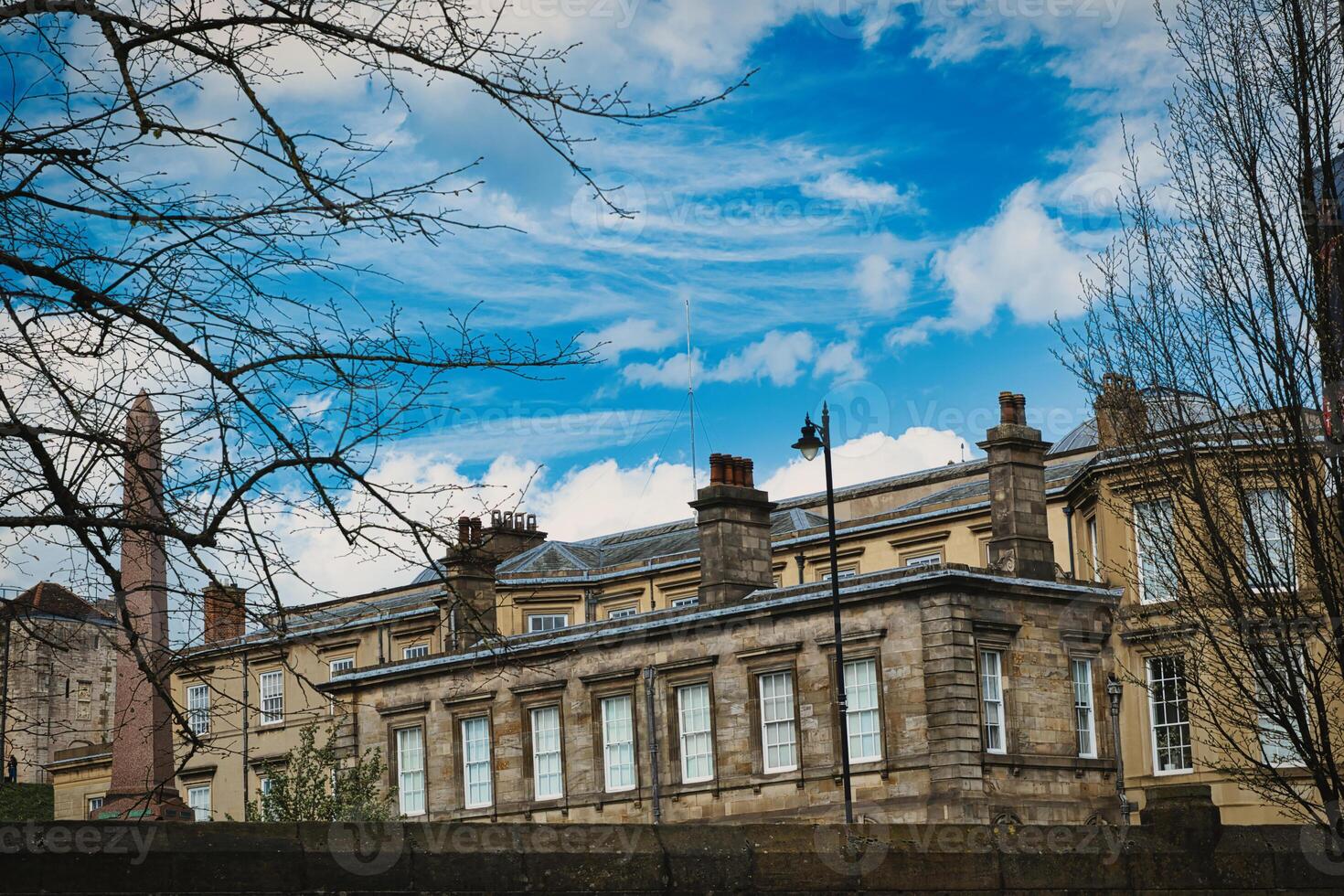 Classic European architecture with ornate details under a vibrant blue sky with fluffy clouds, framed by bare tree branches on the left in York, North Yorkshire, England. photo