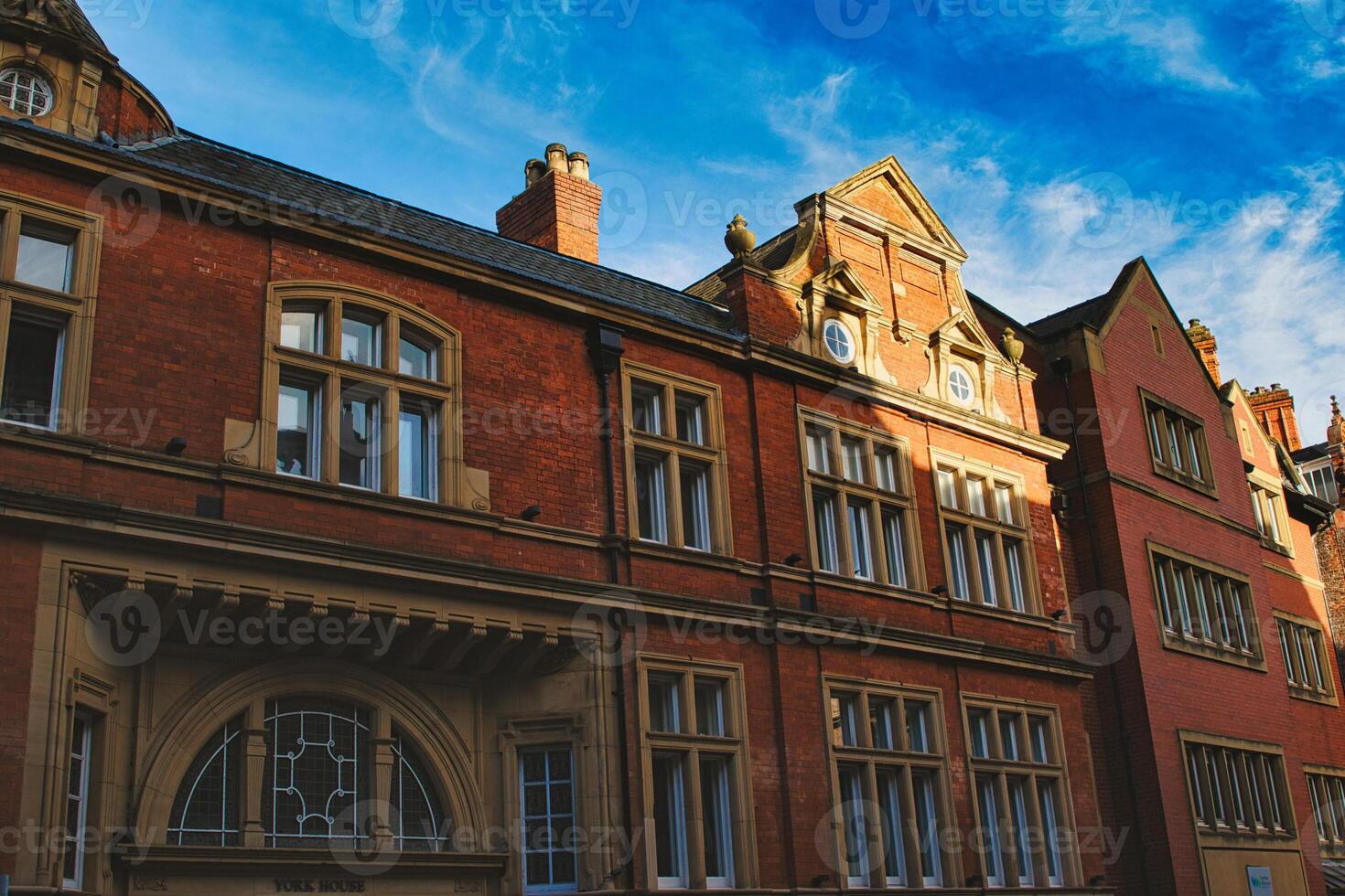 Traditional red brick building with ornate windows under a clear blue sky, showcasing classic architectural details and warm sunlight casting shadows in York, North Yorkshire, England. photo