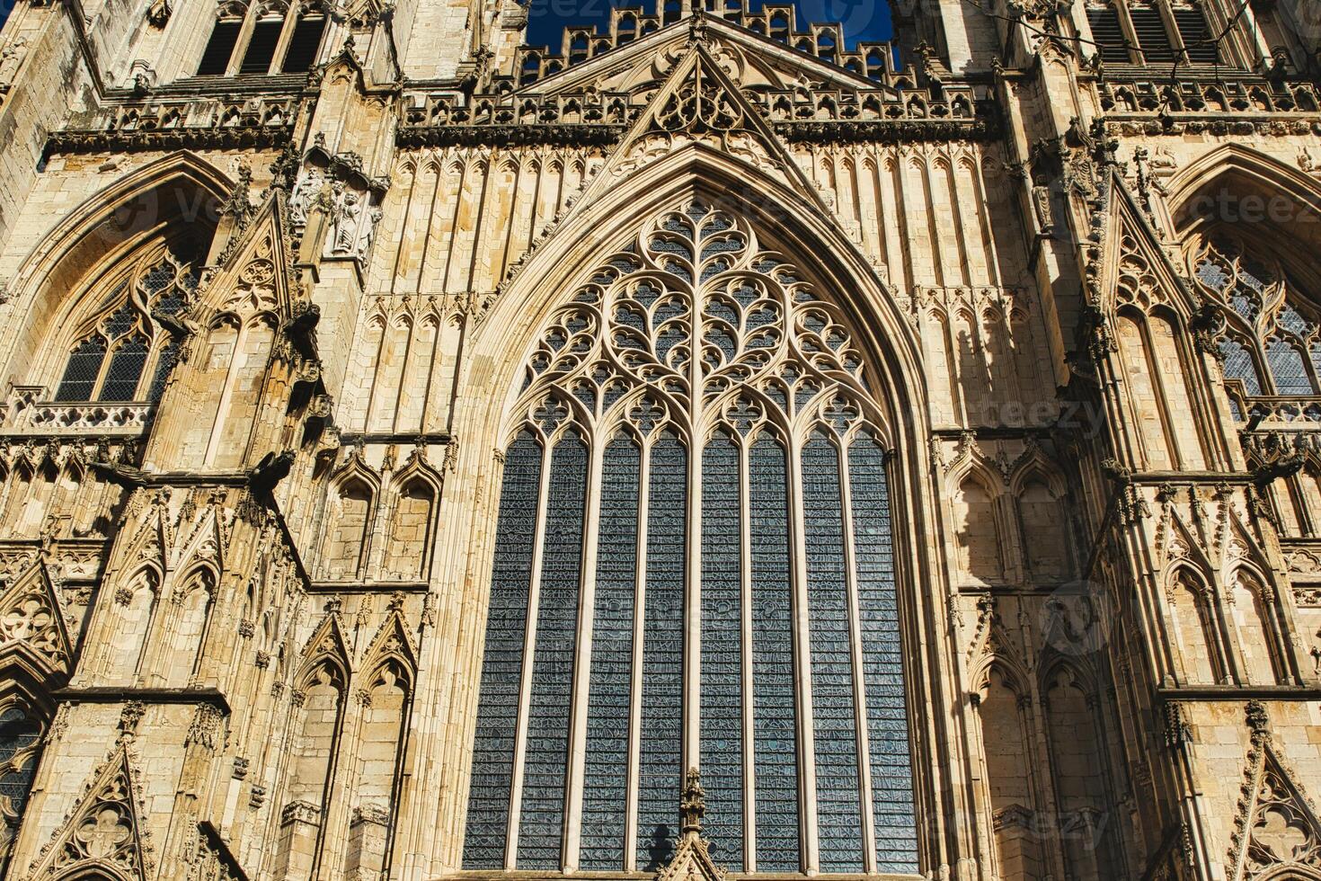 Gothic architecture detail of a cathedral's facade, featuring a large stained glass window and ornate stone carvings under clear skies in York, North Yorkshire, England. photo