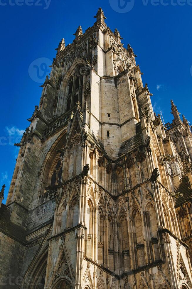 Gothic cathedral facade with intricate architecture against a clear blue sky, showcasing historical religious building's exterior details in York, North Yorkshire, England. photo