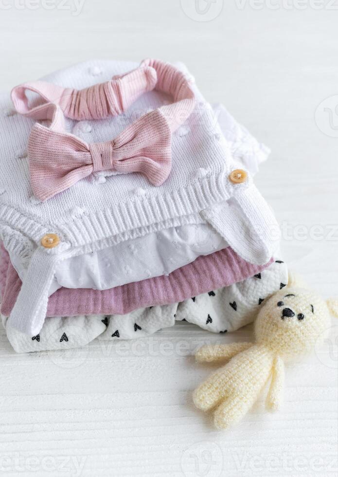 Stack of baby clothes, pink headband and knitted toy bunny. photo