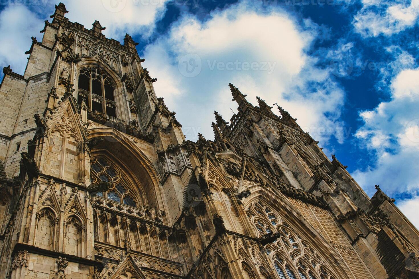 Gothic cathedral's facade with intricate stone carvings against a vivid blue sky with fluffy clouds, showcasing architectural grandeur and historical elegance in York, North Yorkshire, England. photo