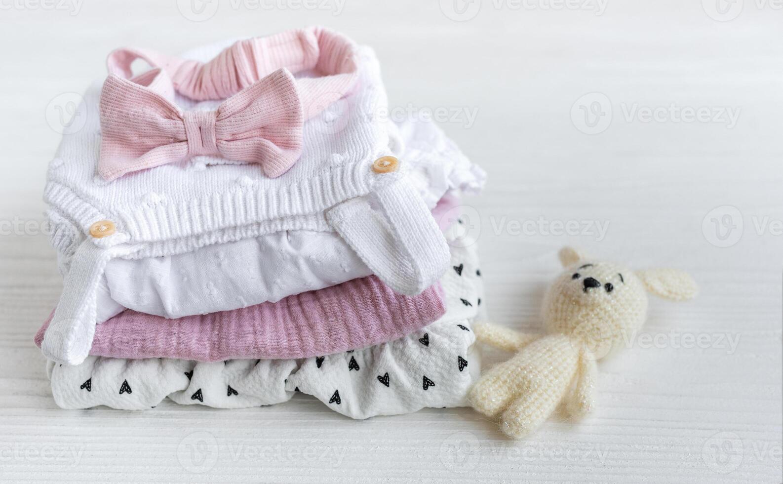 Stack of baby clothes, pink headband and knitted toy bunny. photo