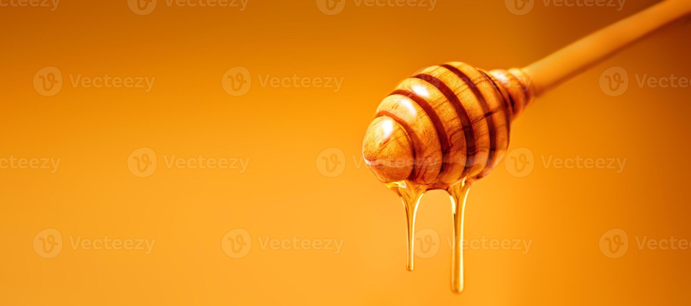 Honey dripping from wooden honey dipper over yellow background. Sweet bee product for your design with copyspace. photo