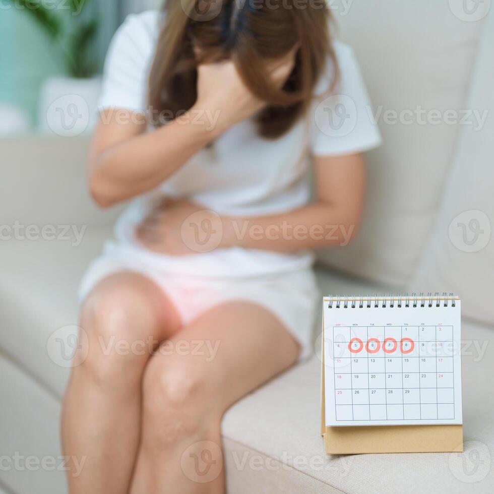 Menstruation period cycle of monthly and Stomachache concepts. woman having abdomen pain with calendar, illness female suffer from premenstrual ache and body Health problem on sofa at home photo