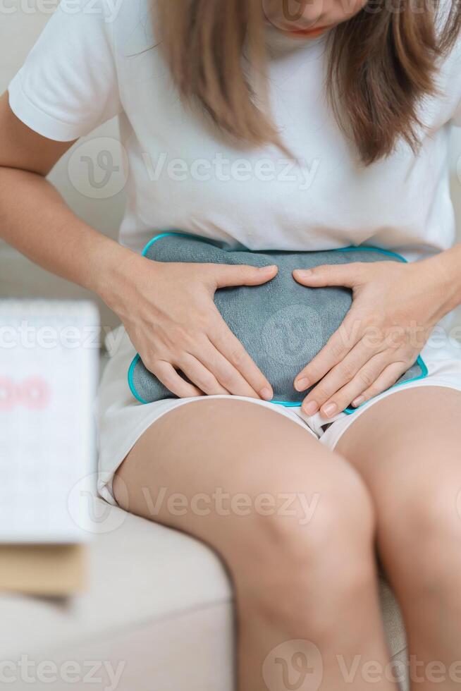 Menstruation period cycle of monthly and Stomachache concepts. woman having abdomen pain with hot water bottle and calendar, illness female suffer from premenstrual ache and body Health problem photo