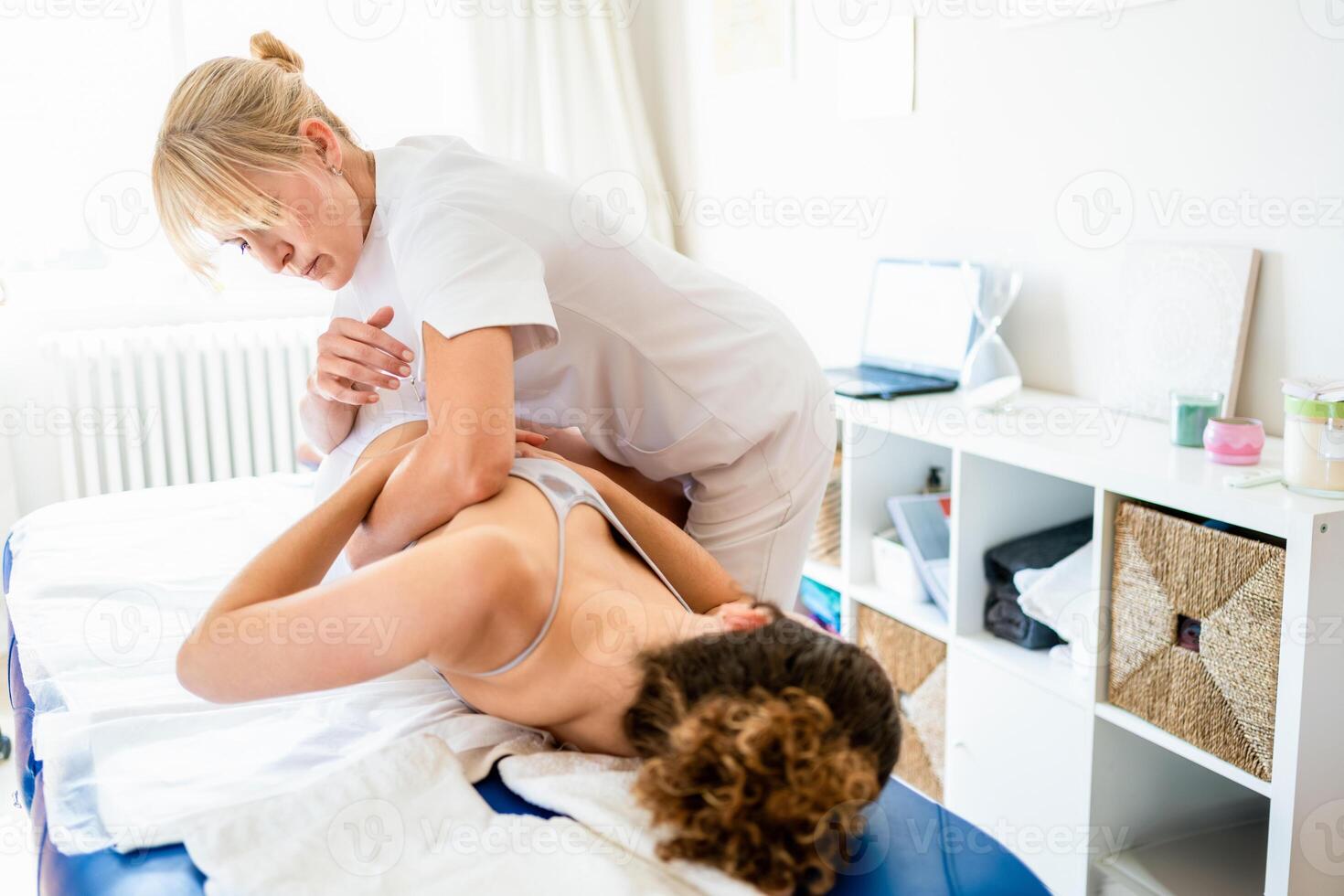 Female physical therapist doing spinal manipulation on patient photo