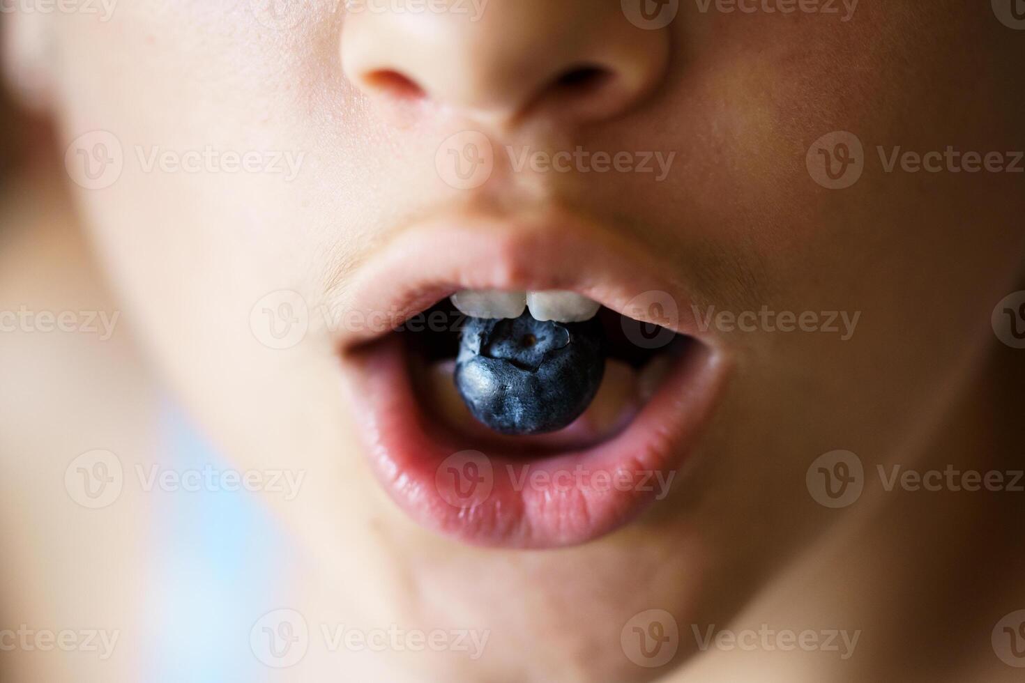 Anonymous teenage girl holding organic blueberry between teeth photo