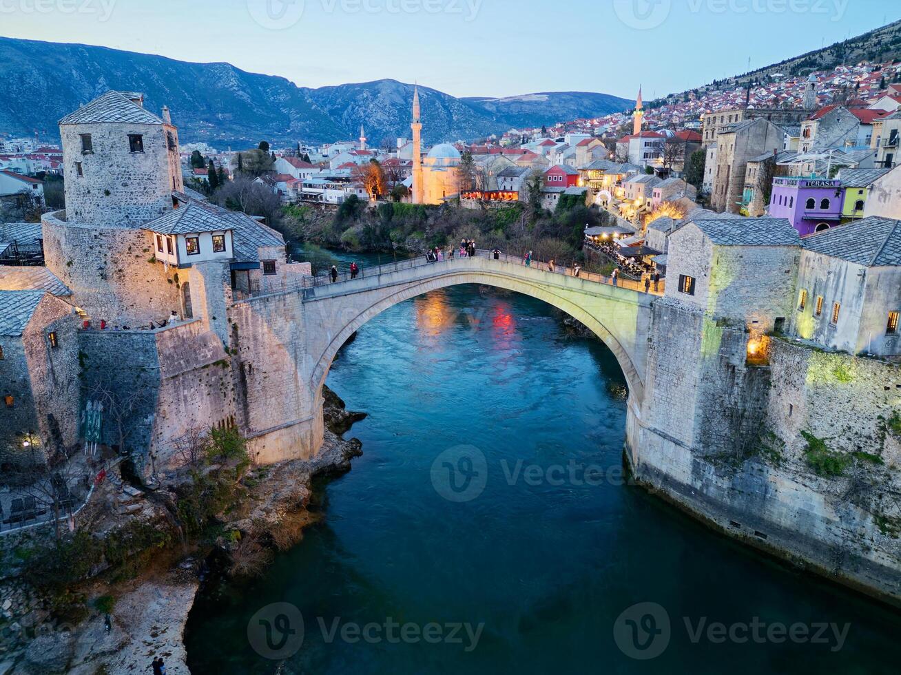 Twilight view of the Old Bridge in Mostar city in Bosnia and Herzegovina. Neretva river. Unesco World Heritage Site. People walking over the bridge. photo