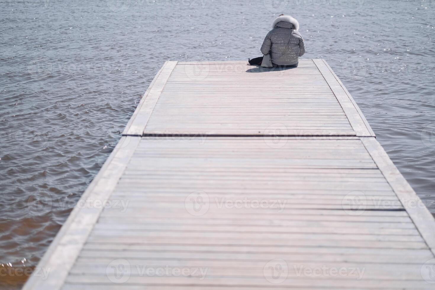 A man is sitting on a wooden pier and looking at the lake. photo