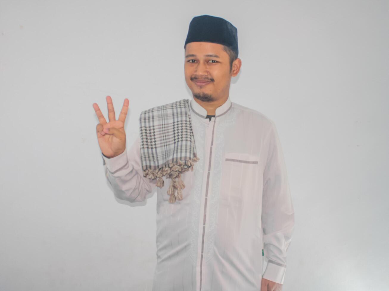 Moslem Asian man smiling at the camera and showing three fingers sign photo
