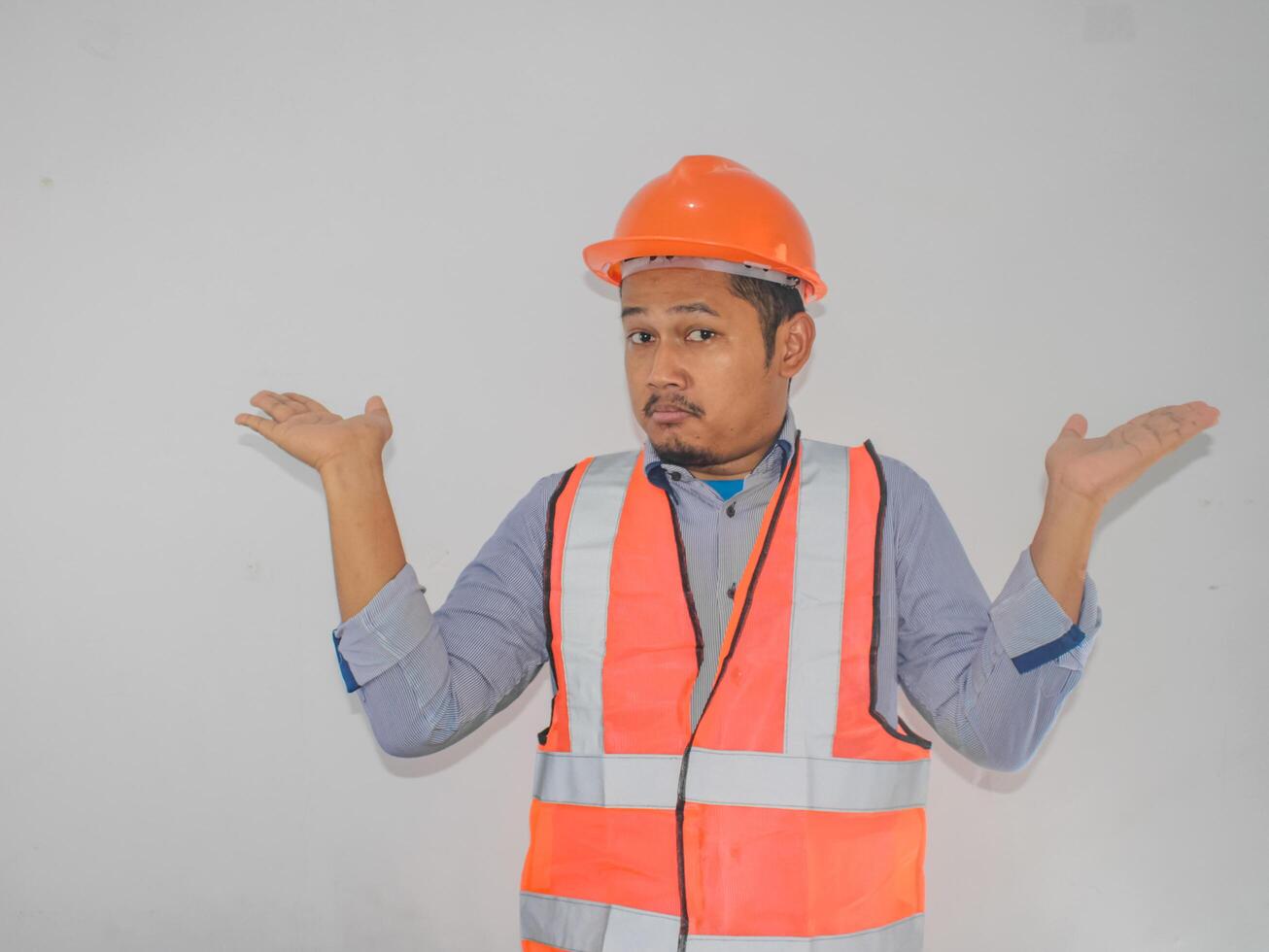 asian worker man wearing orange safety vest uniform and helmet clueless and confused expression with arms and hands raised. Doubt concept. photo