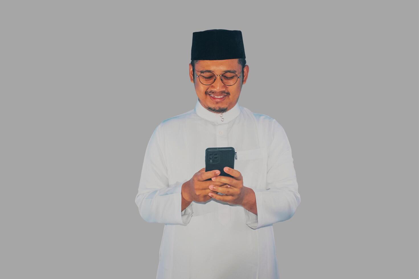 Moslem Asian man smiling happy when texting using his mobile phone photo