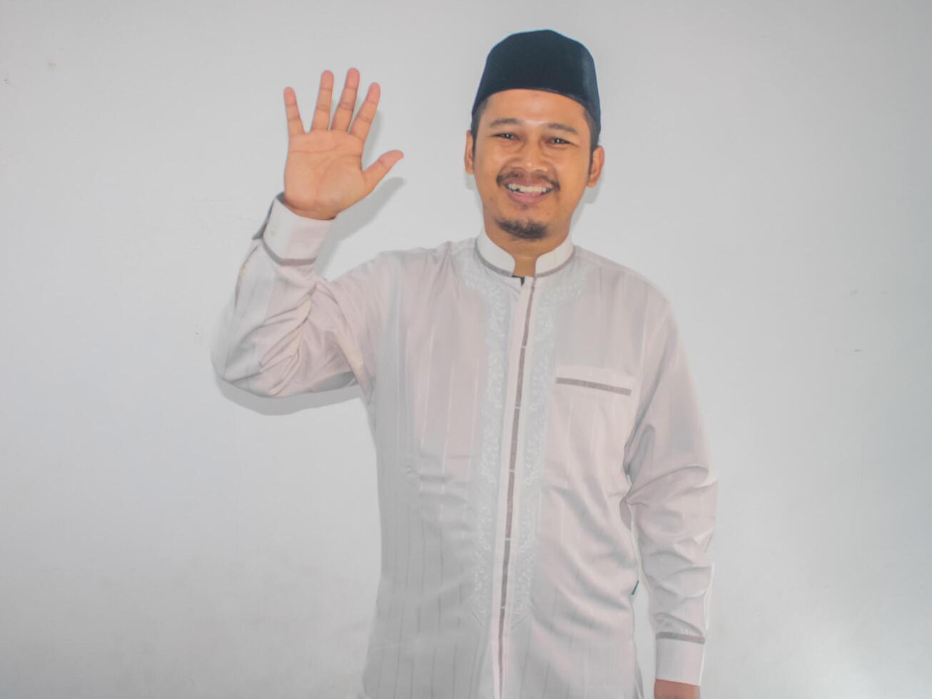 Moslem Asian man showing happy expression when waving hand to greet someone photo