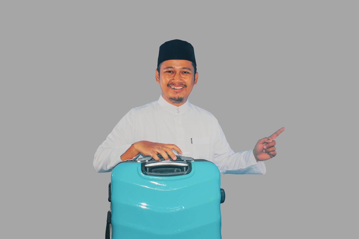 Moslem Asian man smiling at the camera and pointing to the right side while carrying suitcase photo