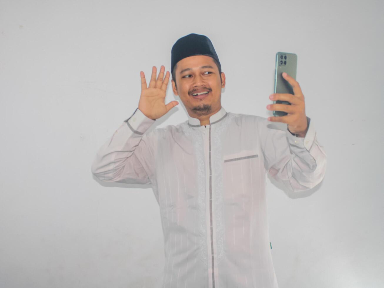 Moslem Asian man waving hand with happy face when doing call with his family photo