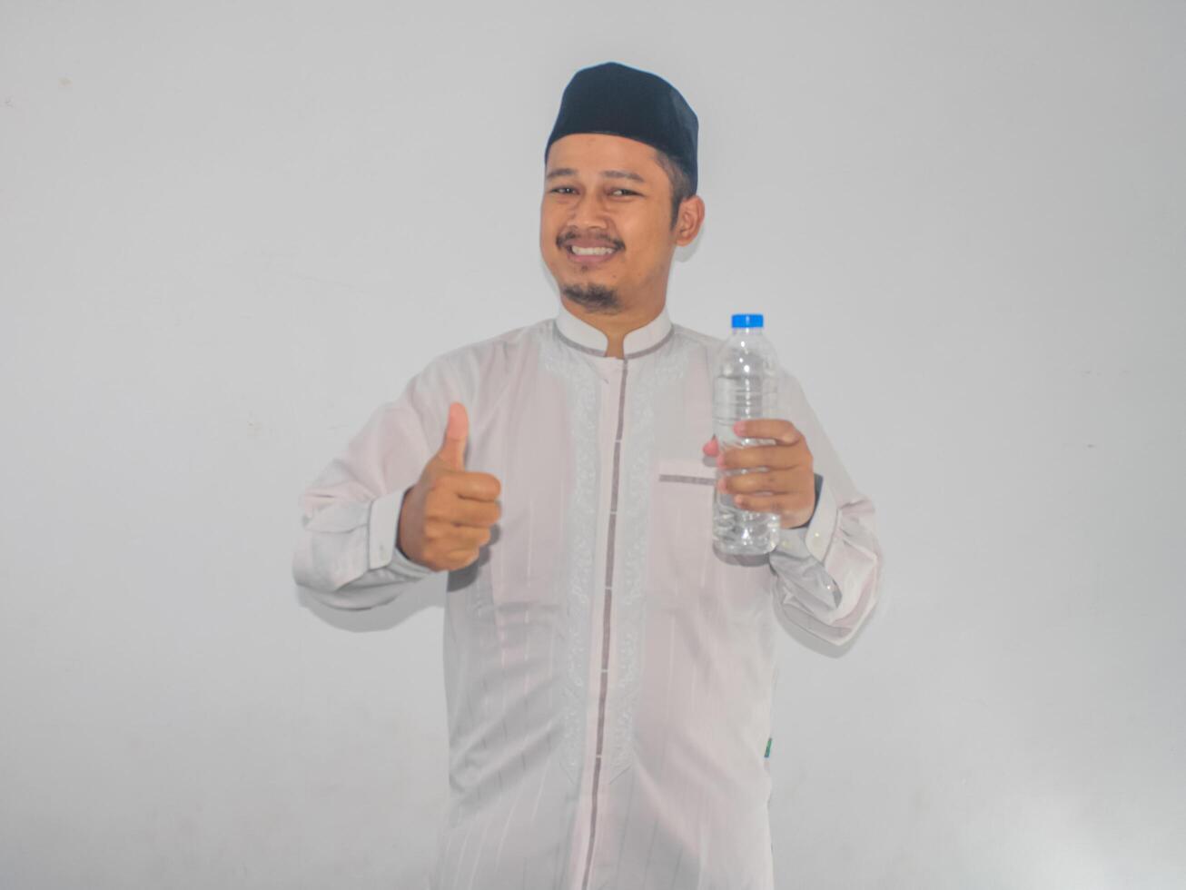 Moslem man smiling while holding a bottle of drinking water and give thumb up photo
