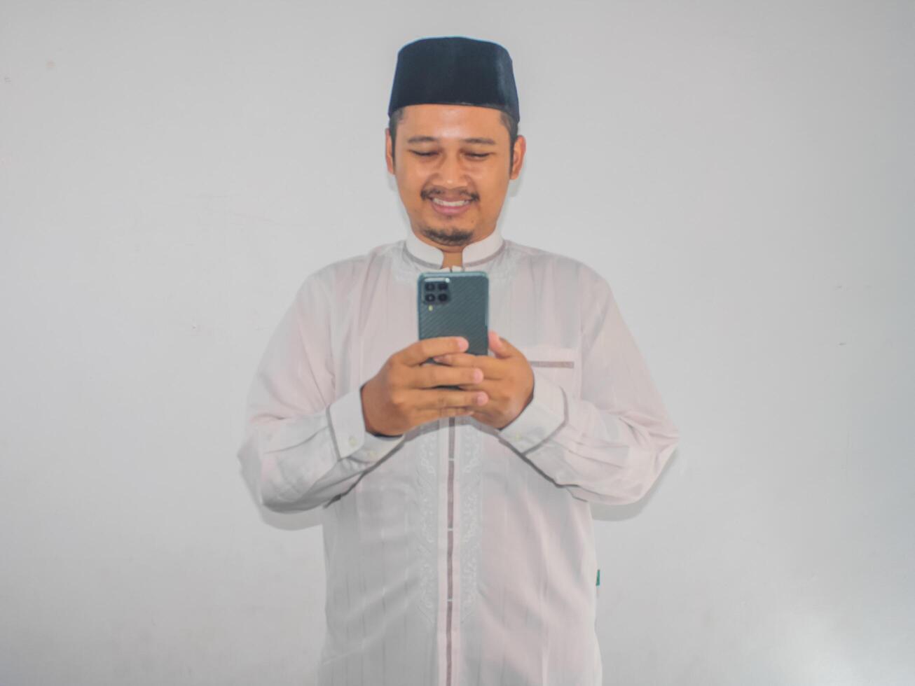 Moslem Asian man smiling happy when texting using his mobile phone photo