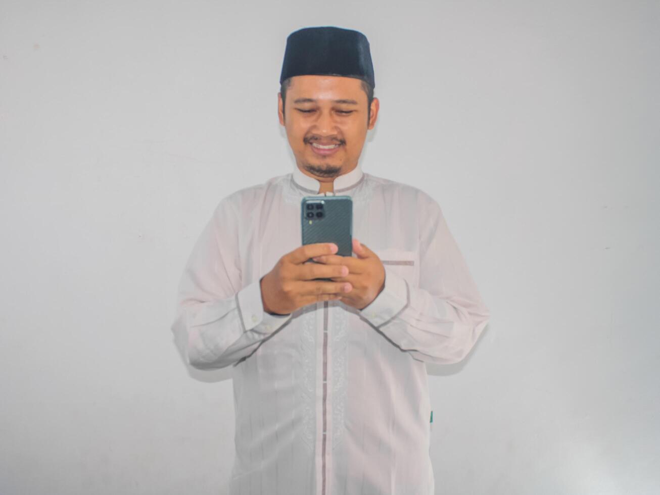 Moslem Asian man smiling happy when texting using his mobile phone photo