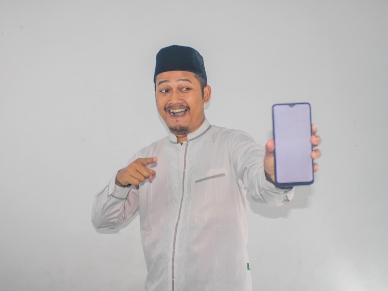 Moslem Asian man smiling and pointing to blank mobile phone screen that he hold photo