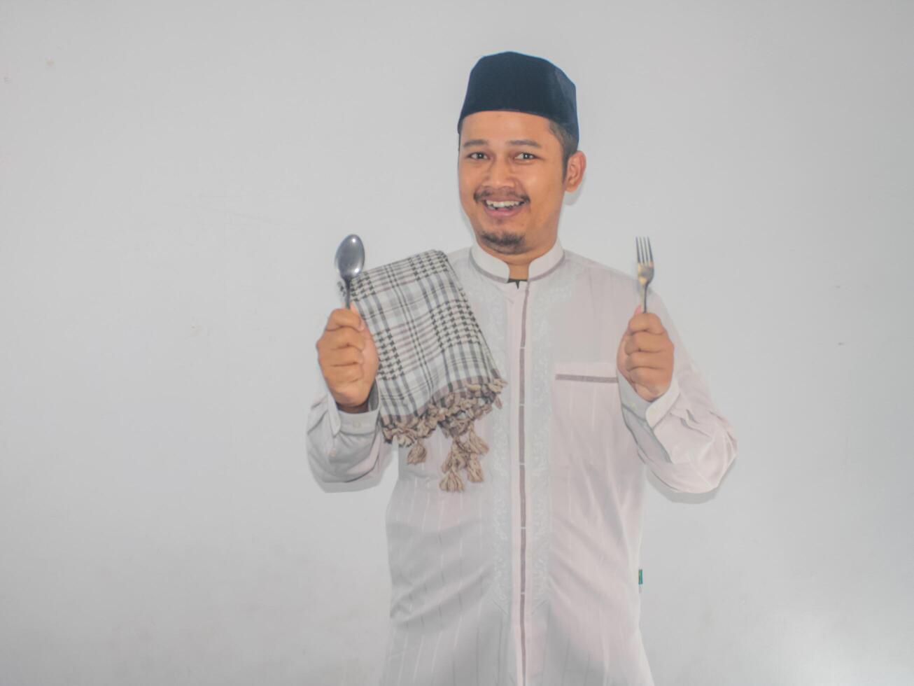 Moslem Asian man smiling happy with hand holding dinning spoon and fork photo