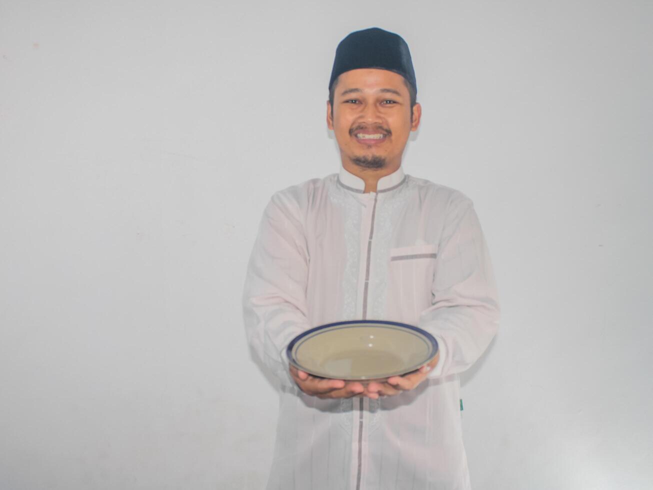 Moslem Asian man smiling happy while holding empty dinner plate photo