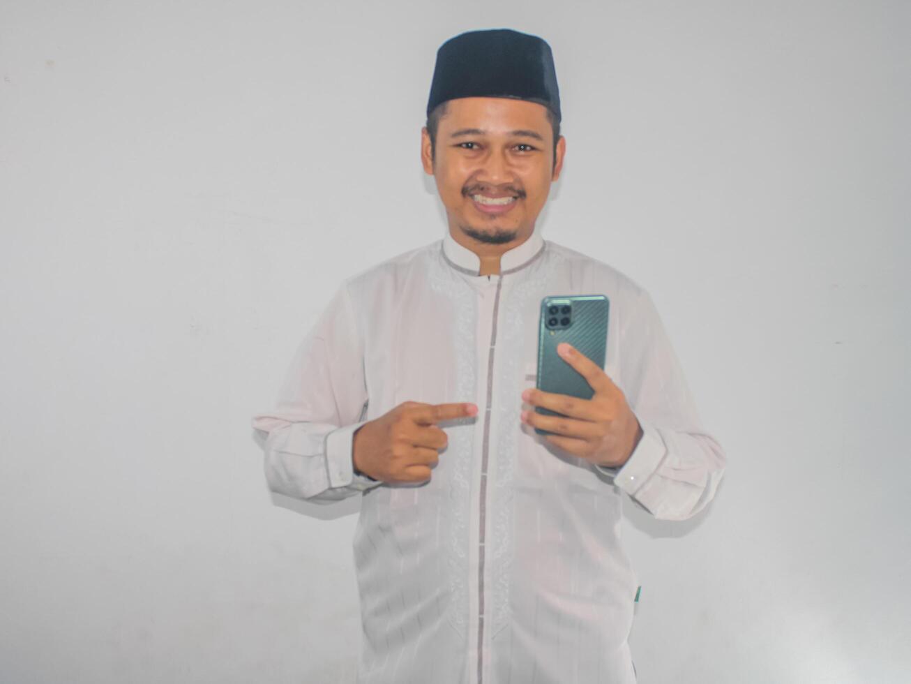 Moslem Asian man smiling and pointing to mobile phone that he hold photo