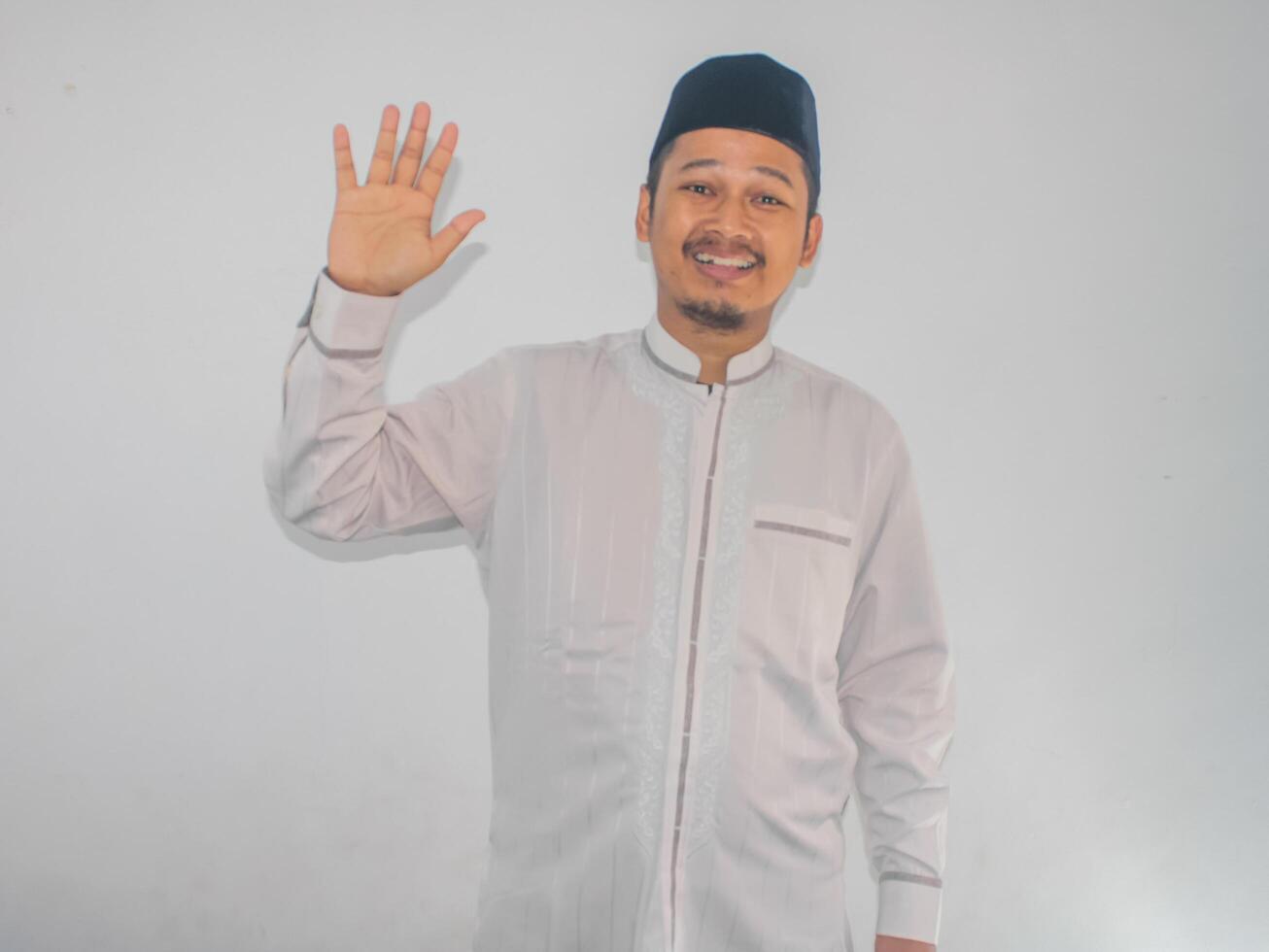 Moslem Asian man showing happy expression when waving hand to greet someone photo