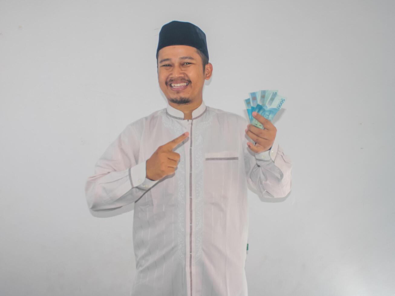 Adult Muslim Asian man smiling and showing confident when pointing to paper money that he hold photo