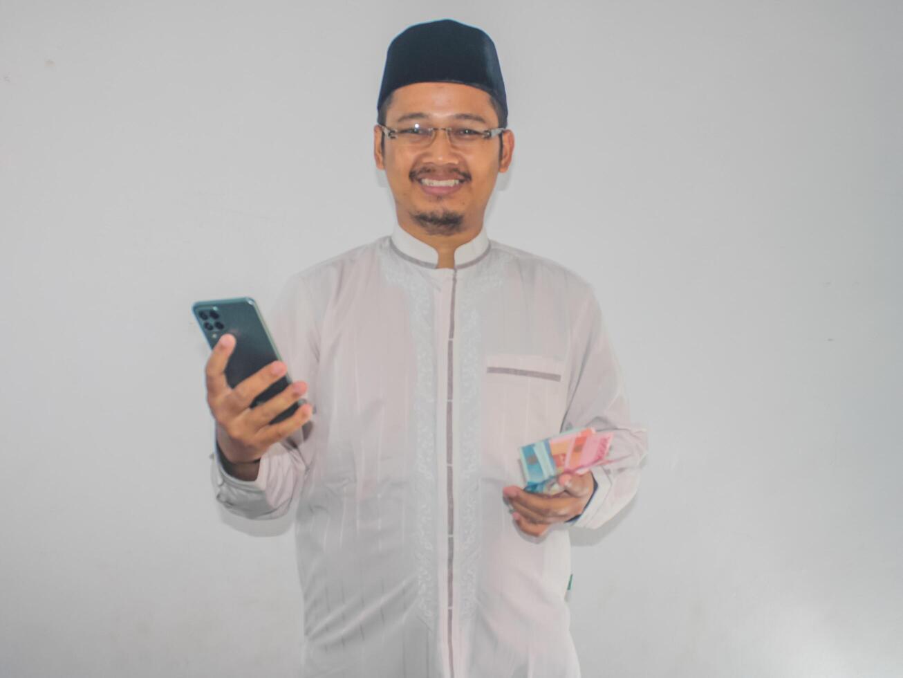 Moslem Asian man smiling happy while holding mobile phone and money photo