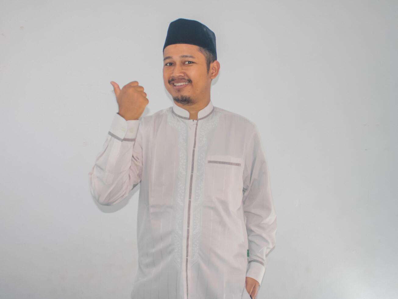 Moslem Asian man smiling at the camera and pointing to the right side with his thumb photo