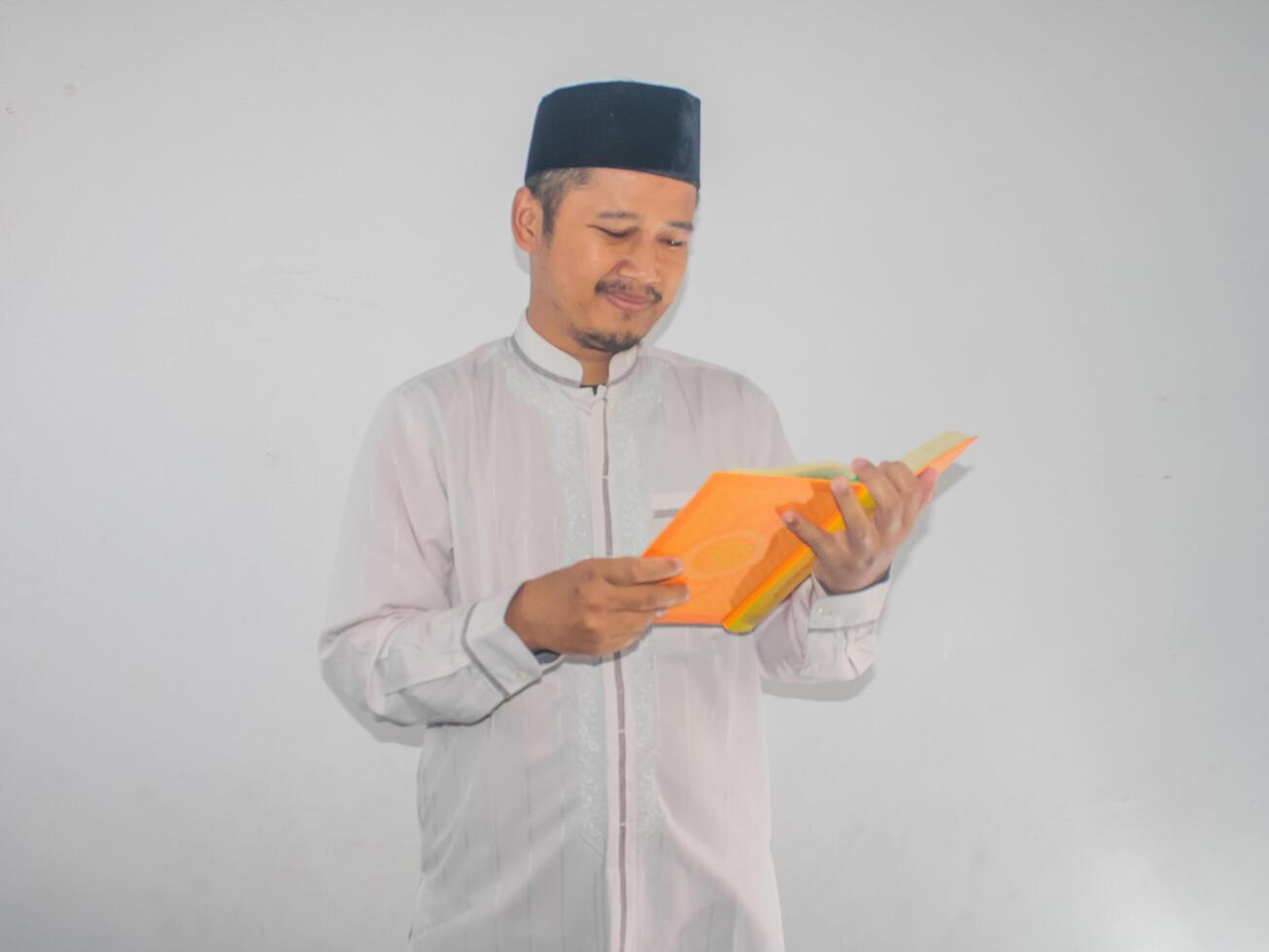 Moslem Asian man smiling at the Al Qur'an and while holding a Al-Qur'an photo
