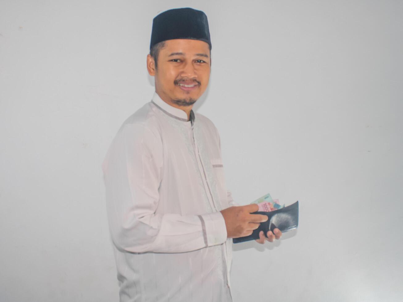 Side view of Moslem Asian man smiling happy when taking money from inside his wallet photo