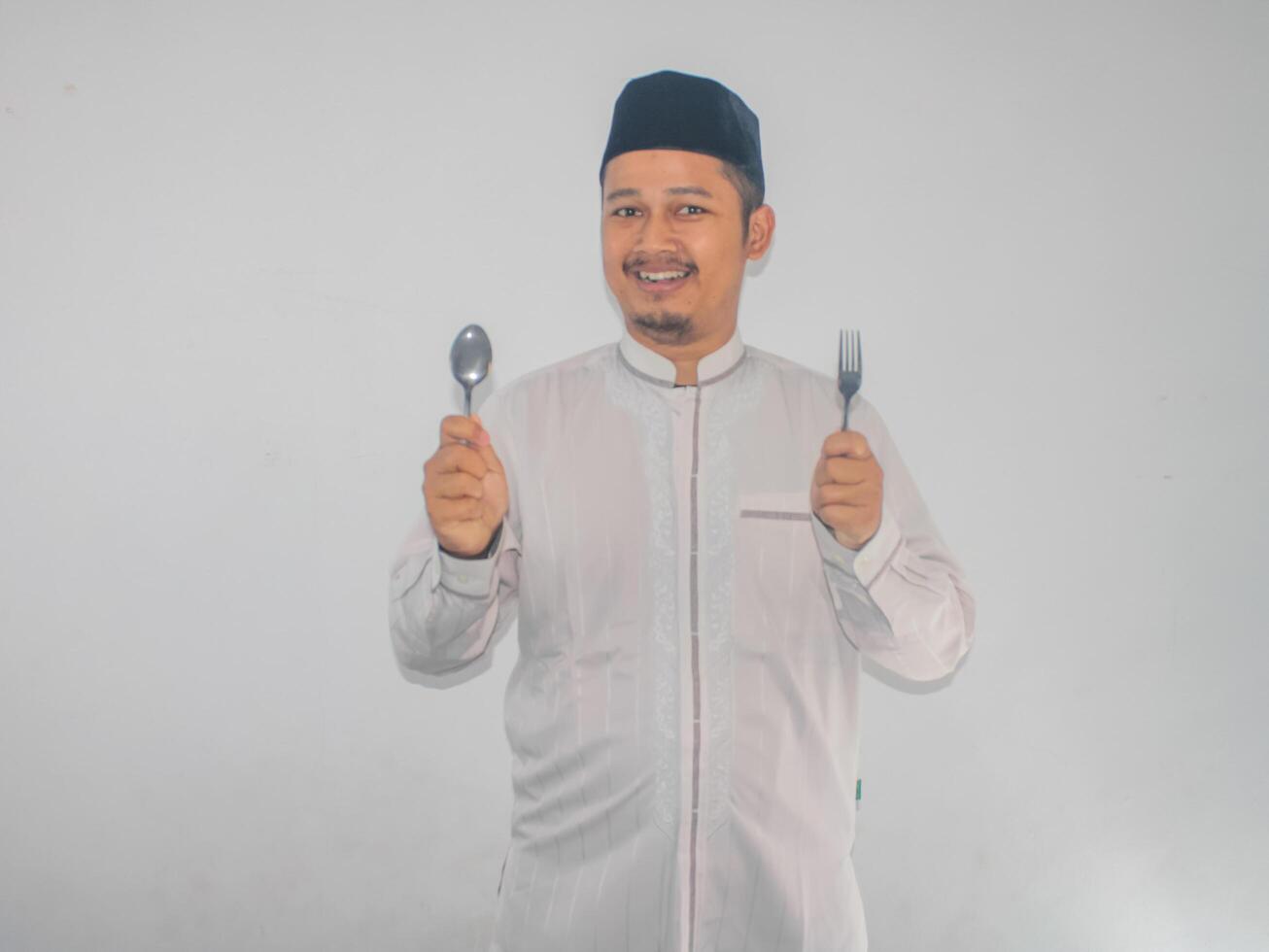 Moslem Asian man smiling happy with hand holding dinning spoon and fork photo