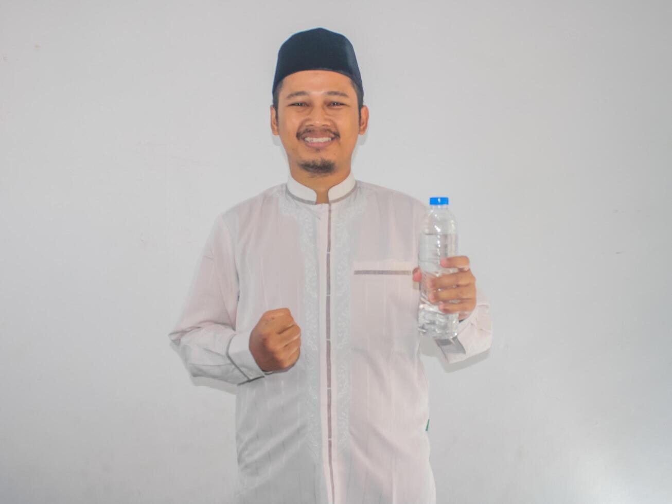 Moslem Asian man smiling at the camera while holding a bottle of drinking water photo