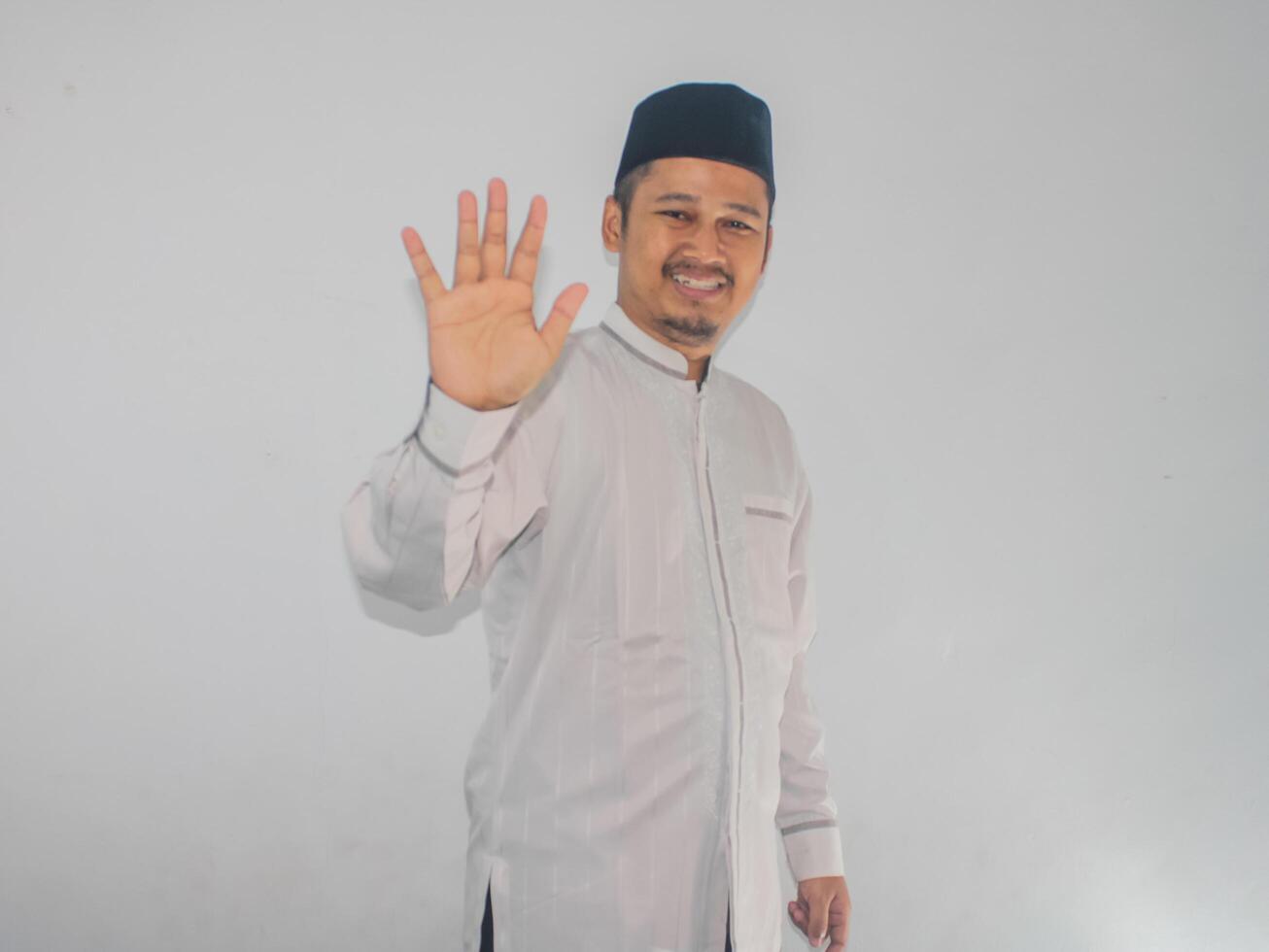 Moslem Asian man showing happy expression when waving hand to greet someone photo