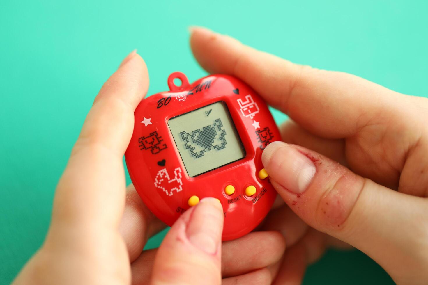 Kyiv, Ucrania - marzo 9, 2024 retro mascota llavero juego tamagotchi en rojo el plastico caso en hembra manos foto