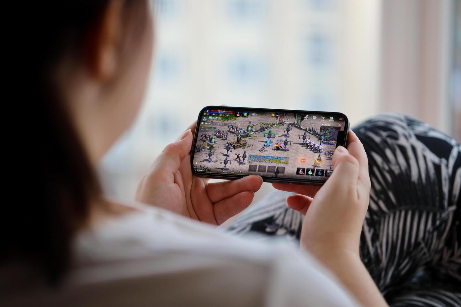 Lineage M mobile iOS game on iPhone 15 smartphone screen in female hands during mobile gameplay photo