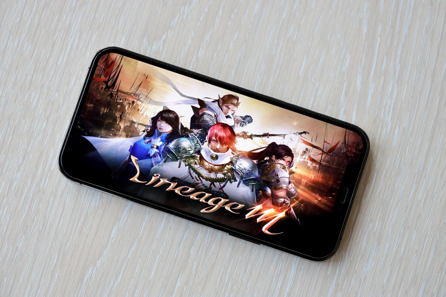 Lineage M mobile iOS game on iPhone 15 smartphone screen on wooden table during mobile gameplay photo