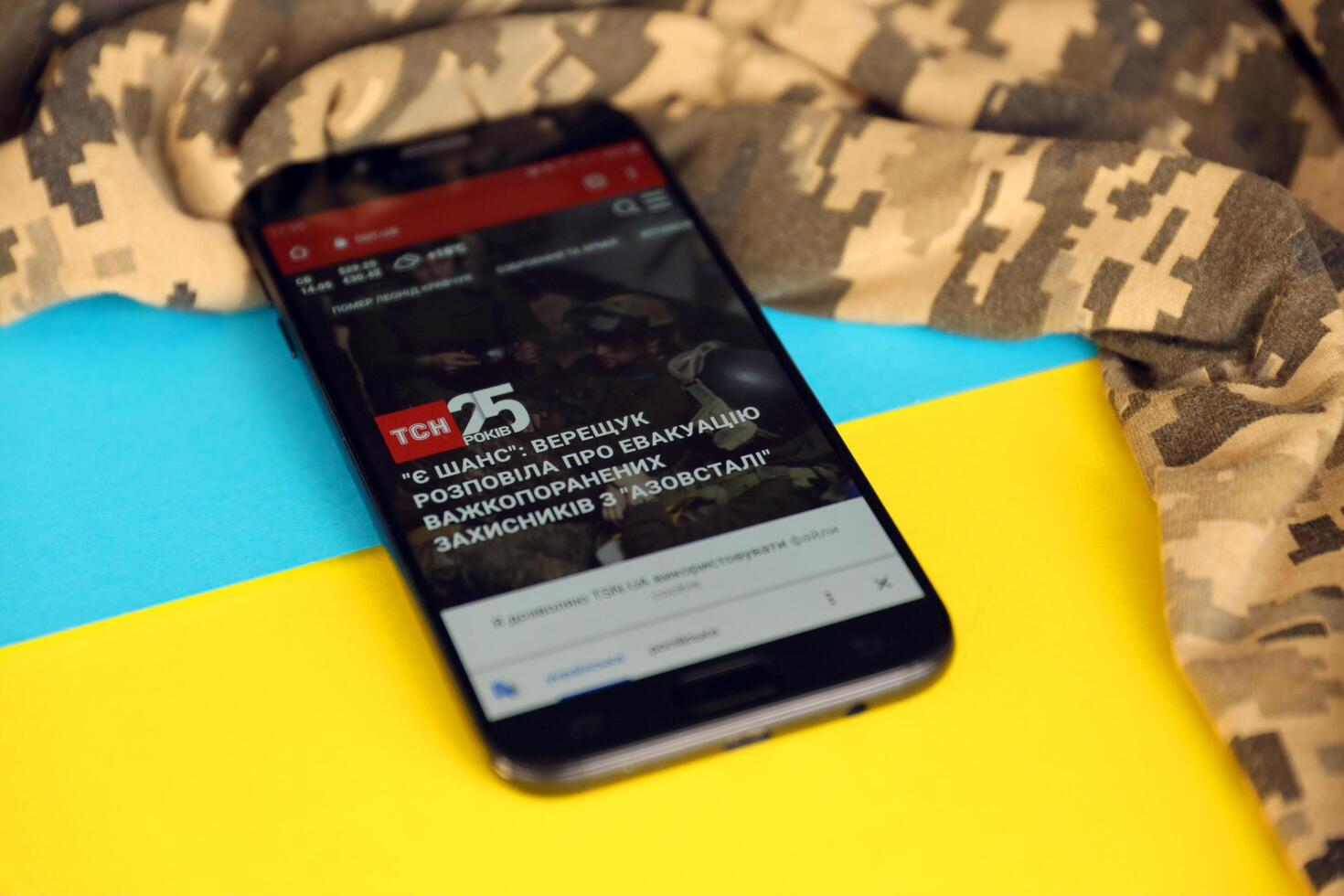 KYIV, UKRAINE - 4 MAY, 2023 TSN ukrainian news portal on smartphone screen with ukrainian flag and camouflage fabric photo