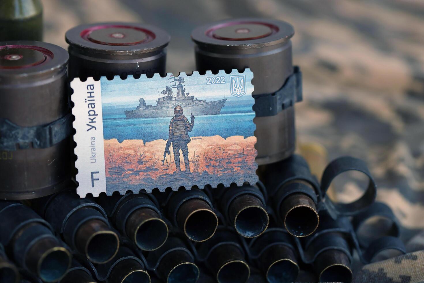 TERNOPIL, UKRAINE - SEPTEMBER 29, 2023 Famous Ukrainian postmark with russian warship and ukrainian soldier as wooden souvenir on army camouflage uniform cloth and machine gun belt photo