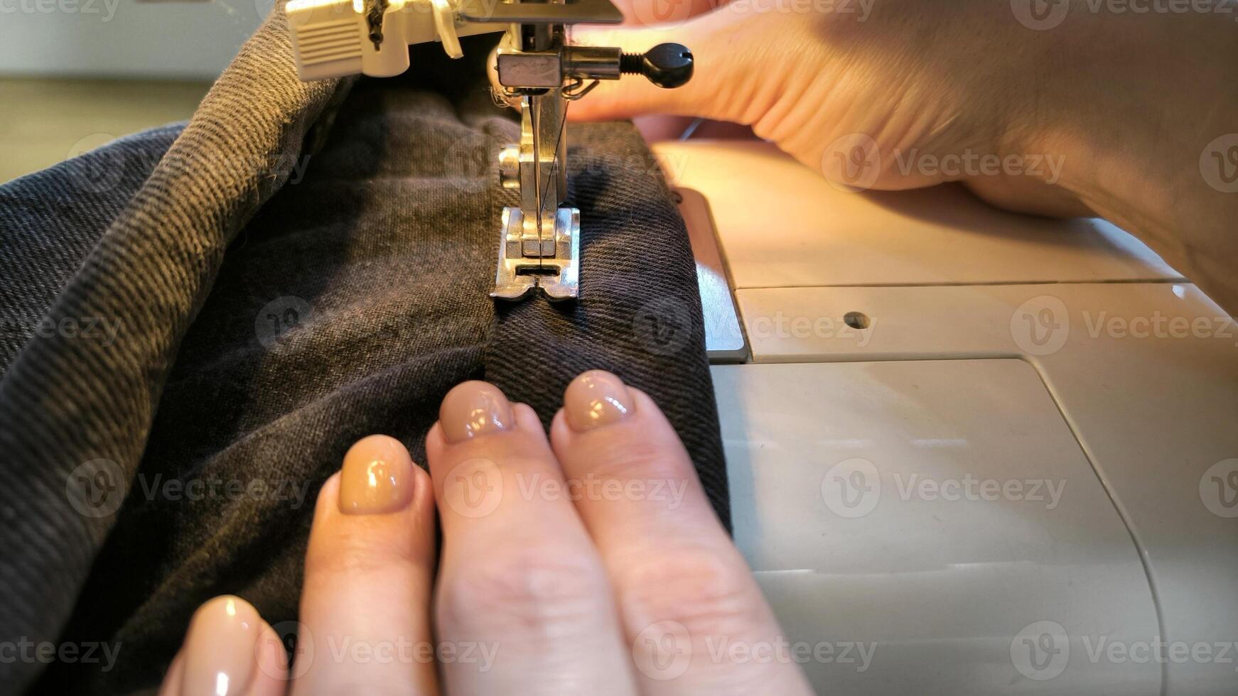 process of sewing in a sewing machine sew woman's hands manicure black textile denim jeans manufacturing close up seamstress in workshop fabric clothes making design hobby handmade working needlework photo