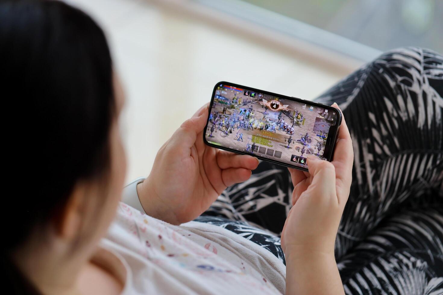 Lineage M mobile iOS game on iPhone 15 smartphone screen in female hands during mobile gameplay photo