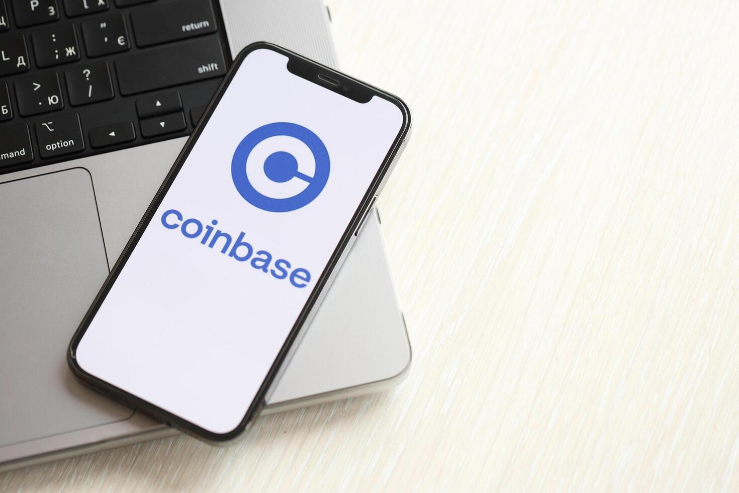 KYIV, UKRAINE - MARCH 15, 2024 Coinbase logo on iPhone display screen on MacBook panel logo on iPhone display screen with dollars and bitcoins on MacBook photo