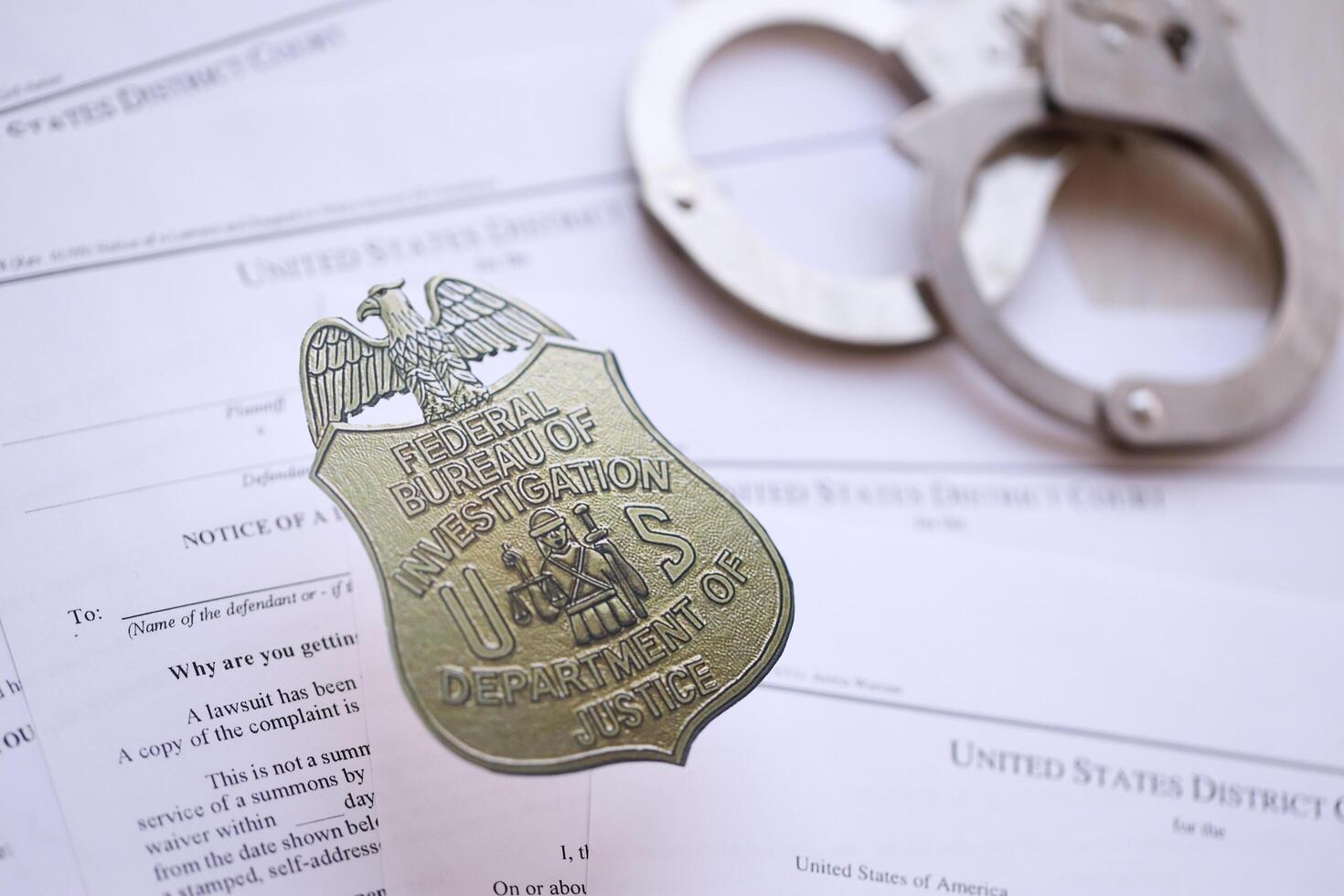 KYIV, UKRAINE - MARCH 9, 2024 US FBI Federal Bureau of Investigation badge with handcuffs on many US District Court warrants and complaints photo