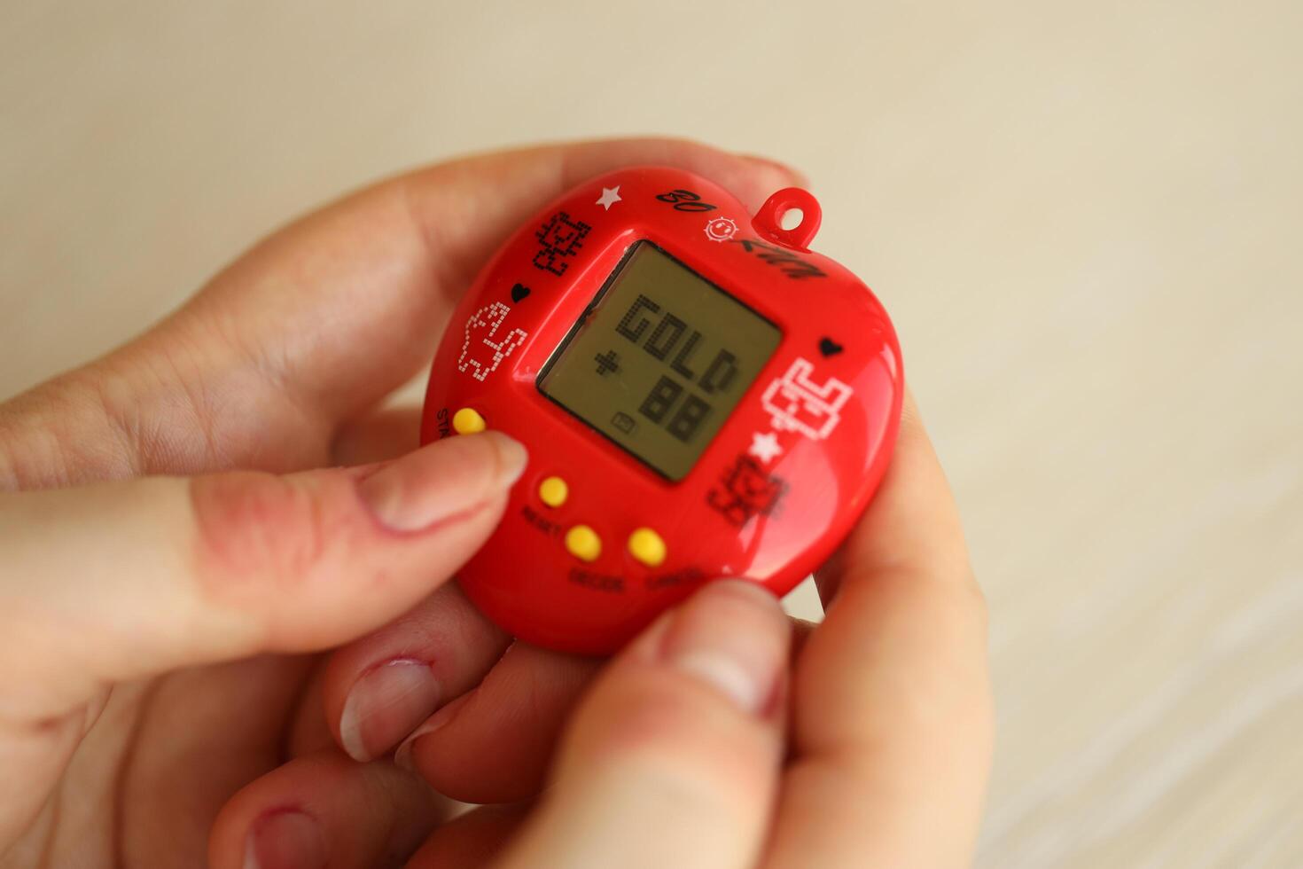 KYIV, UKRAINE - MARCH 9, 2024 Retro pet keychain game tamagotchi in red plastic case in female hands photo